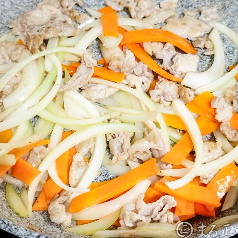 豚肉に火が通ったら玉ねぎとニンジンを加えて炒めます。
